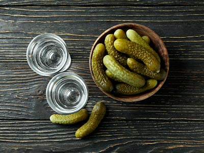 Two shots of vodka and a bowl of pickles on a table