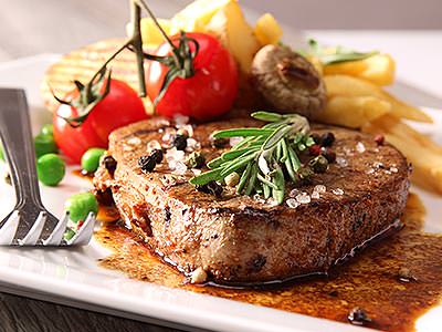 A steak topped with leaves and sea salt, with chips and tomatos in the background, served up on a white plate