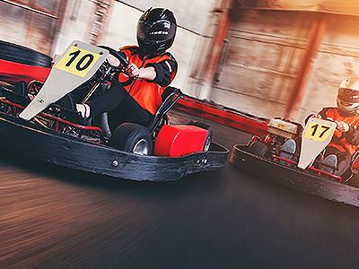 The front of two people in go karts, racing on an indoor track