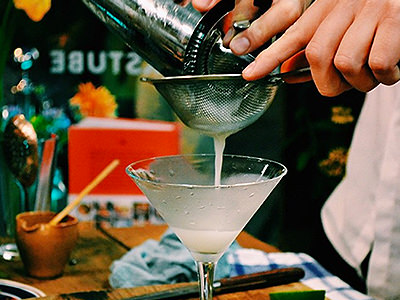 A pale cocktail being double strained into a martini glass