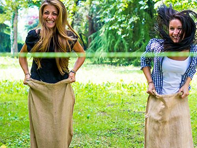 Two women in sacks, jumping and racing outside to a green ribbon