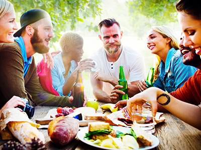 Six people sitting on a picnic bench outside, eating food and drinking from bottles