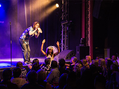 Someone performing on stage in front of a large crowd and a bride at a Comedy Club in Bath