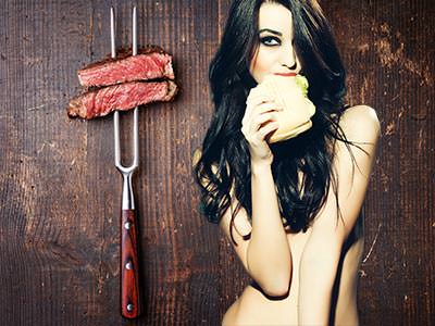 Two pieces of uncooked meat on a BBQ skewer and a naked girl eating a burger