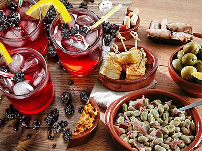 Split image of red cocktails topped with lemons and ice, and Spanish tapas dishes on a table