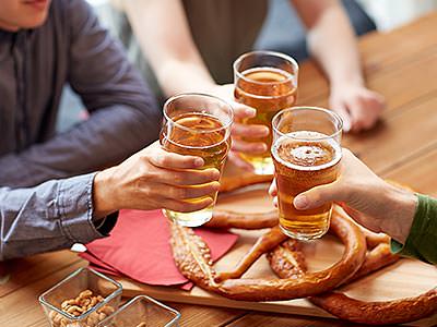 Three men raise glasses of beer together over a platter of pretzels