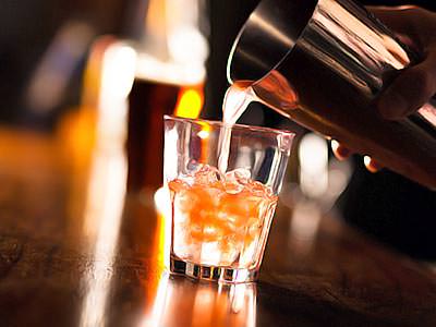 An orange drink being poured from a metal cocktail shaker into a glass