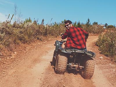 A man driving a quad bike down a dirt road, looking back at the camera