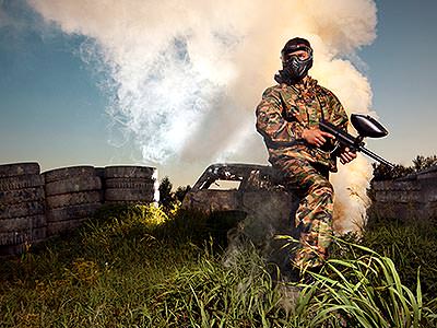 A man wearing camouflage overalls and a mask standing near tyres and a plume of white smoke
