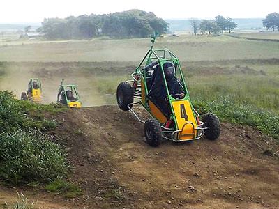 A yellow and green off-road buggy landing after going over a jump on a dirt track