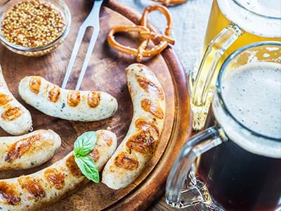 Bratwurst and various other German foood on a wooden board, with two full steins on the side