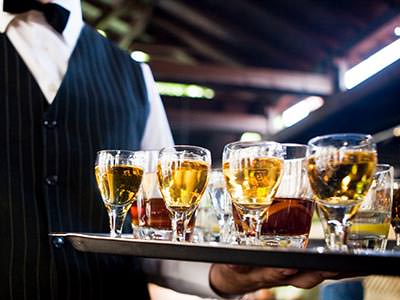 Close up of a waiter in a pinstriped waistcoat, holding a tray of drinks