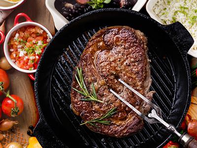 A large steak in a cast iron skillet, being stabbed with a carving fork