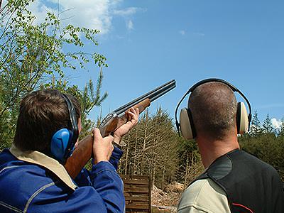 A man aiming with a shotgun to the sky, whilst another man looks on