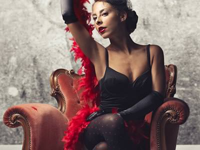 A woman with a feather boa around her, on a red, leather chair 