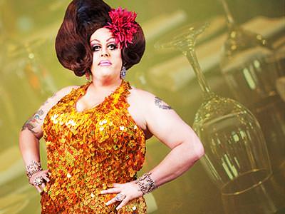 A drag queen with the outline of wine glasses behind her