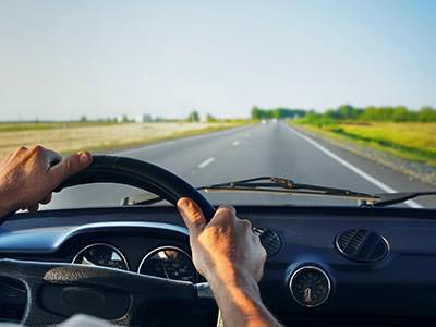 A view from the driver's seat of a vehicle with a long road, steering wheel and hands visible