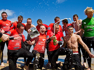 A group of men in red on the beach, celebrating with champagne in Newquay
