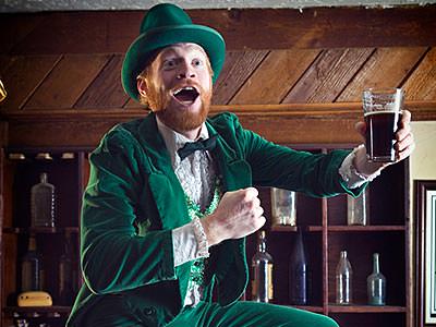 A man in a leprechaun outfit posing with a glass of beer 