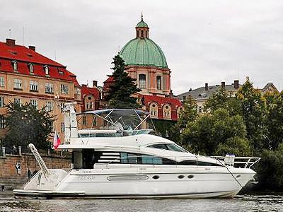 A white boat on the Vltava river, with buildings in the background in Prague