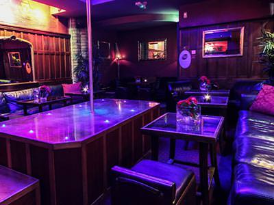 An empty strip club with seating, tables and a podium with a pole