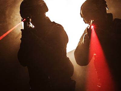 Two men aim guns emitting visible red laser beams past the camera