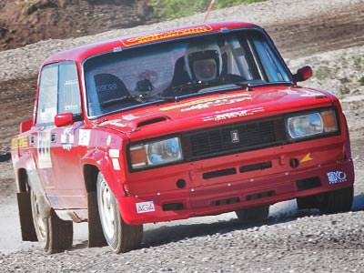 A red Lada car driving on a gravel road
