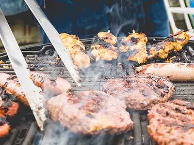 Tongs on a steak on a barbecue, with other meat in the background