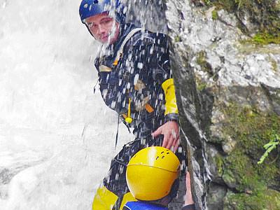 Close up of a man gorge scrambling and being splashed with water in a wetsuit and a helmet