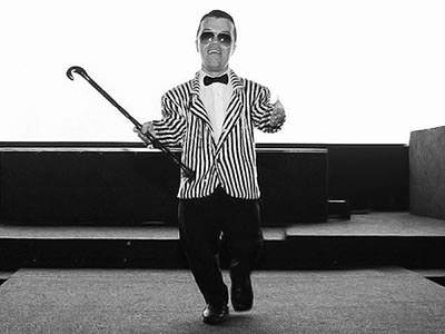 Black and white image of a man with dwarfism wearing a striped jacket and bow tie, and holding a cane