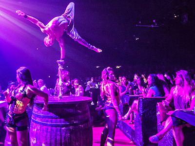 A man balancing on a barrel and performing to a crowd, to a backdrop of purple light