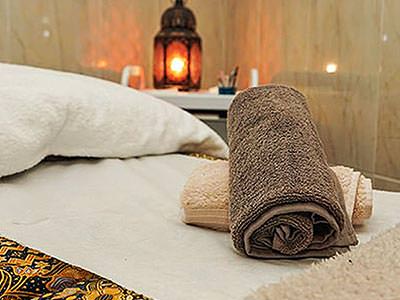 Two rolled-up towels on a bed with a lamp in the background