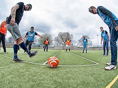 Men wearing goggles and attempting to kick an orange football