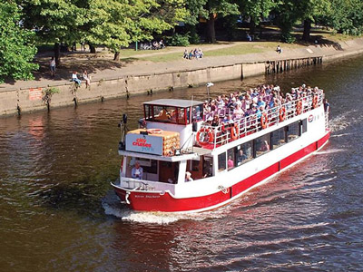 A red and white boat sailing on a river with a bridge and blue sky in the background in York