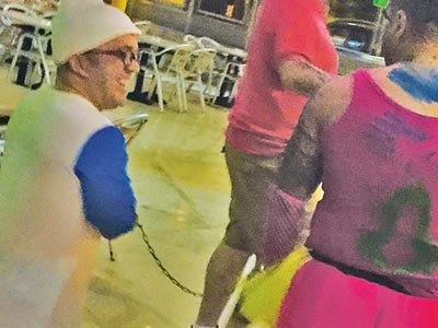 A man with dwarfism dressed as a smurf and attached to a man in a pink vest