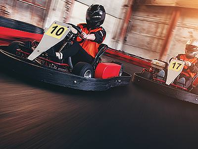 Two people in red overalls, racing go karts on an indoor track