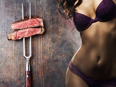 A woman's body in purple underwear, tiled next to a skewer of meat against a wooden table