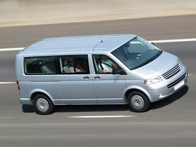 A silver minibus driving on a road