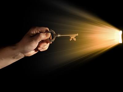 A man's hand holding a key to a light coming through a door