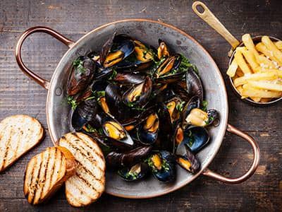 Mussels in a bowl, with bread on the side and a small bowl of chips