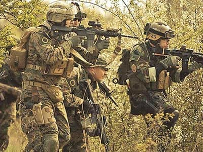 A group of people in camouflage and helmets, firing airsoft rifles in a forest