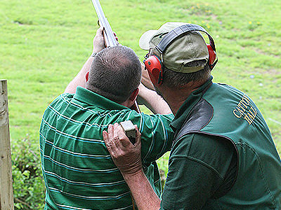 A man aiming with a shotgun with an instructor's aid