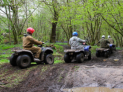 The backs of four men driving quad bikes through a muddy field