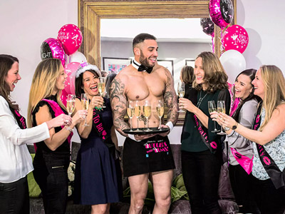 A man dressed in an apron serving drinks to a hen group