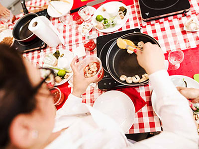 Someone putting some food into a saucepan, on a table with a gingham tablecloth