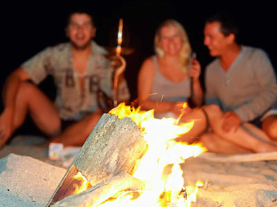 A woman and two men sitting around a camp fire