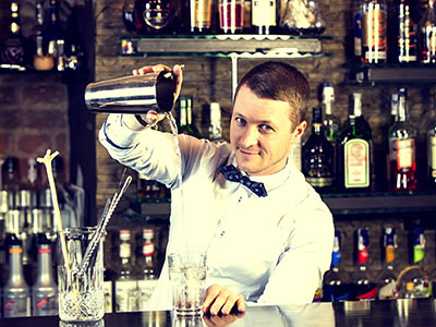 A man behind a bar pouring a drink into a glass from a cocktail shaker