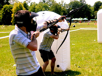 Two people hiding behind an inflatable obstacle, holding bows with rubber tipped arrows