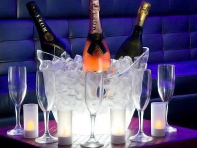 Three bottles of alcohol in an ice bucket on a table, with wine glasses around it