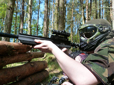 A person dressed in camouflage holding a paintball gun in a forest 